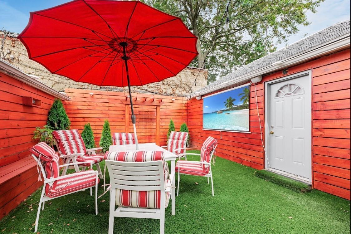 A patio with a table and chairs and a red umbrella.