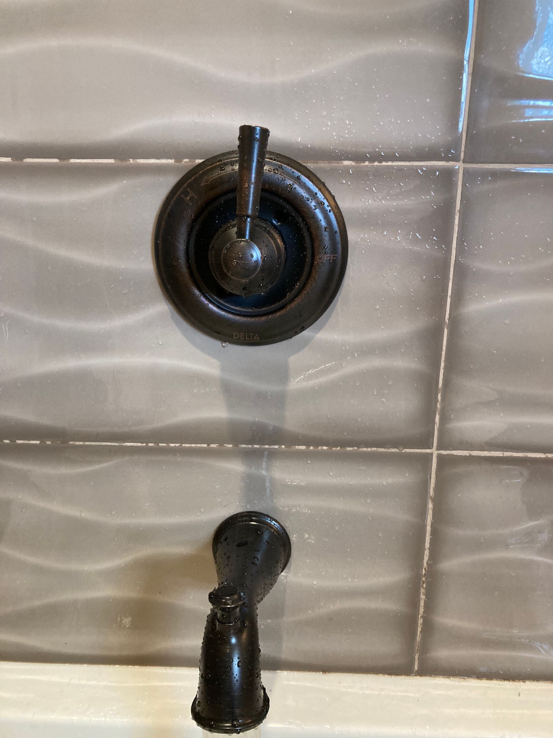 A close up of a shower faucet on a tiled wall.