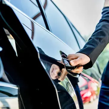 Person in suit opening the door of a black car.