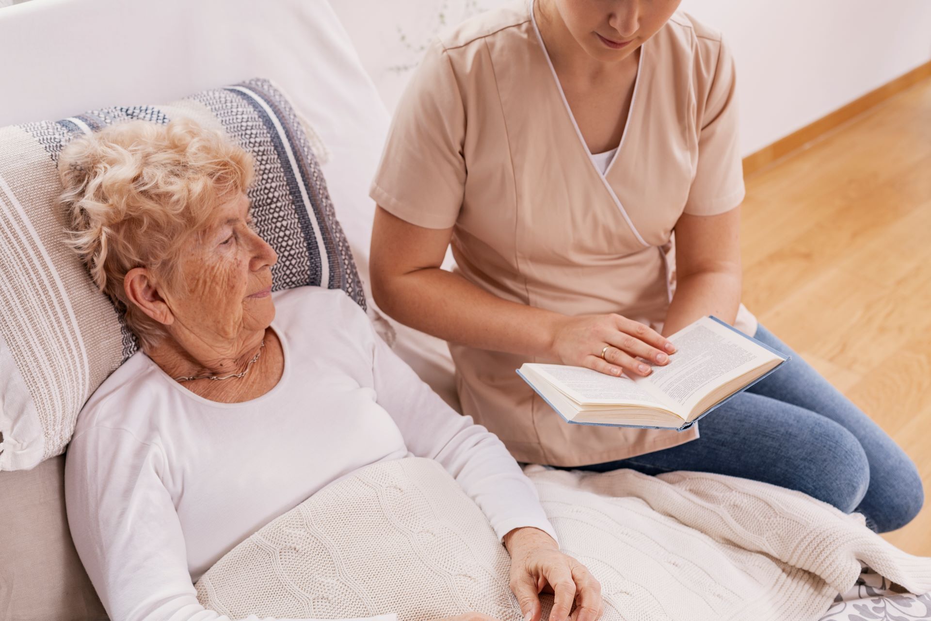 caregiver reads book to woman on hospital bed