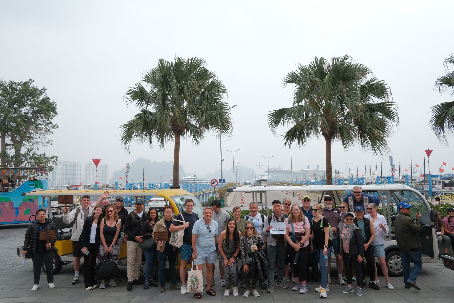 A group of international tourists posing together in front of palm trees and colorful decorations during a tour with Up Travel Vietnam.