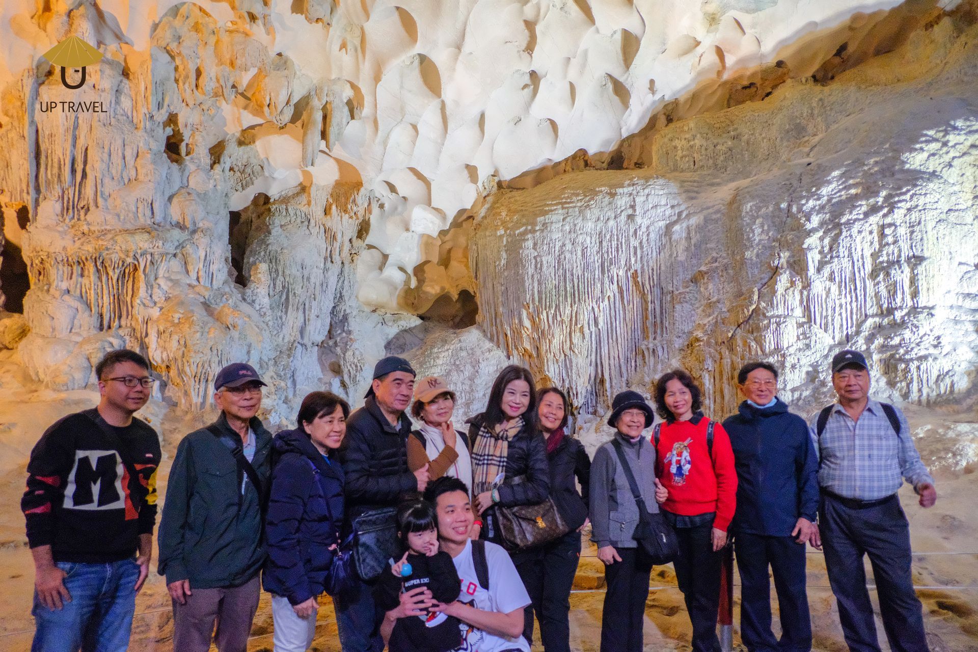 A group of tourists exploring a magnificent limestone cave in Ha Long Bay, surrounded by illuminated stalactites and stalagmites.