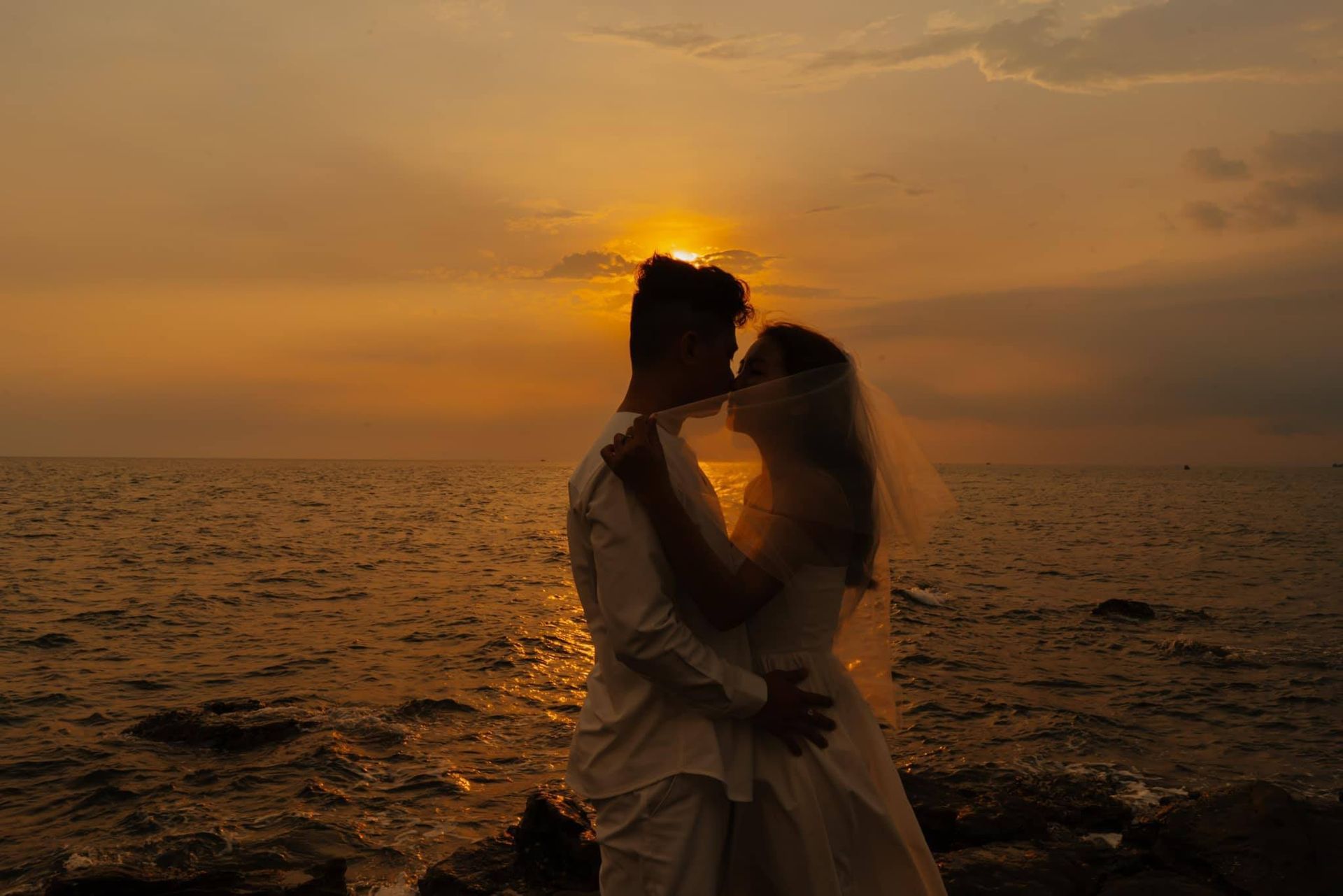 A couple shares a romantic sunset kiss by the sea, capturing the perfect wedding moment in Vietnam.