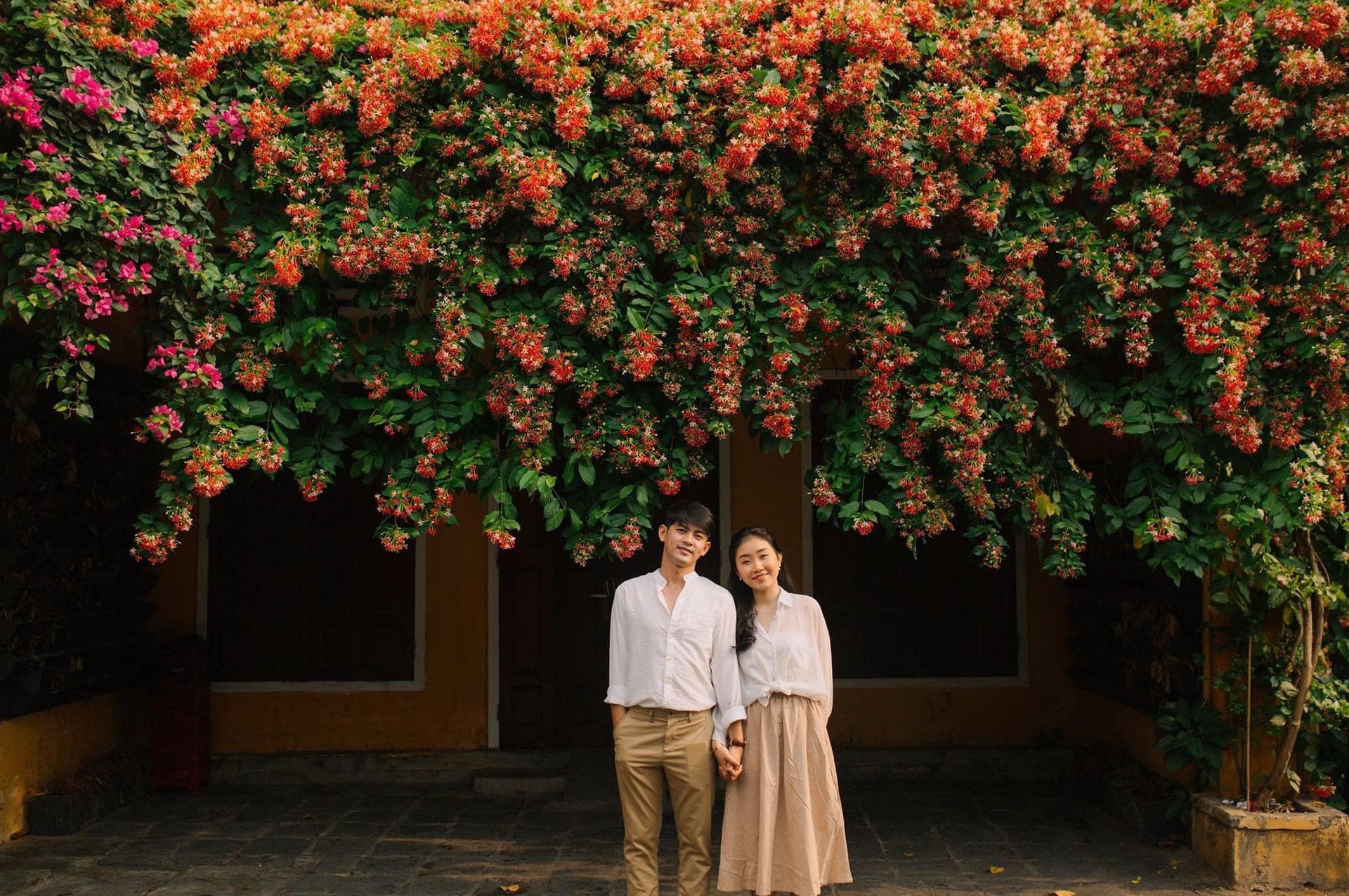 A couple under vibrant bougainvillea in Hoi An, a top romantic destination with ancient charm.