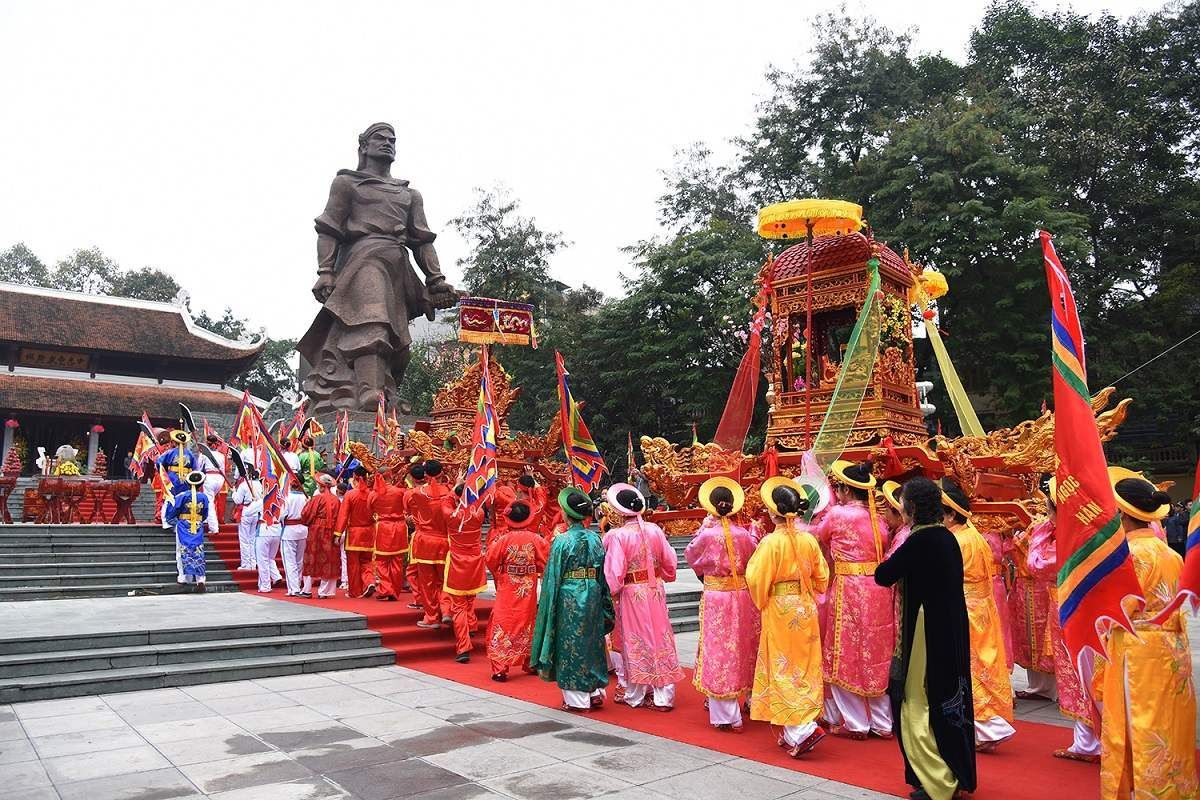 traditional Vietnamese festival procession in colorful costumes, walking past a large statue of King Quang Trung.