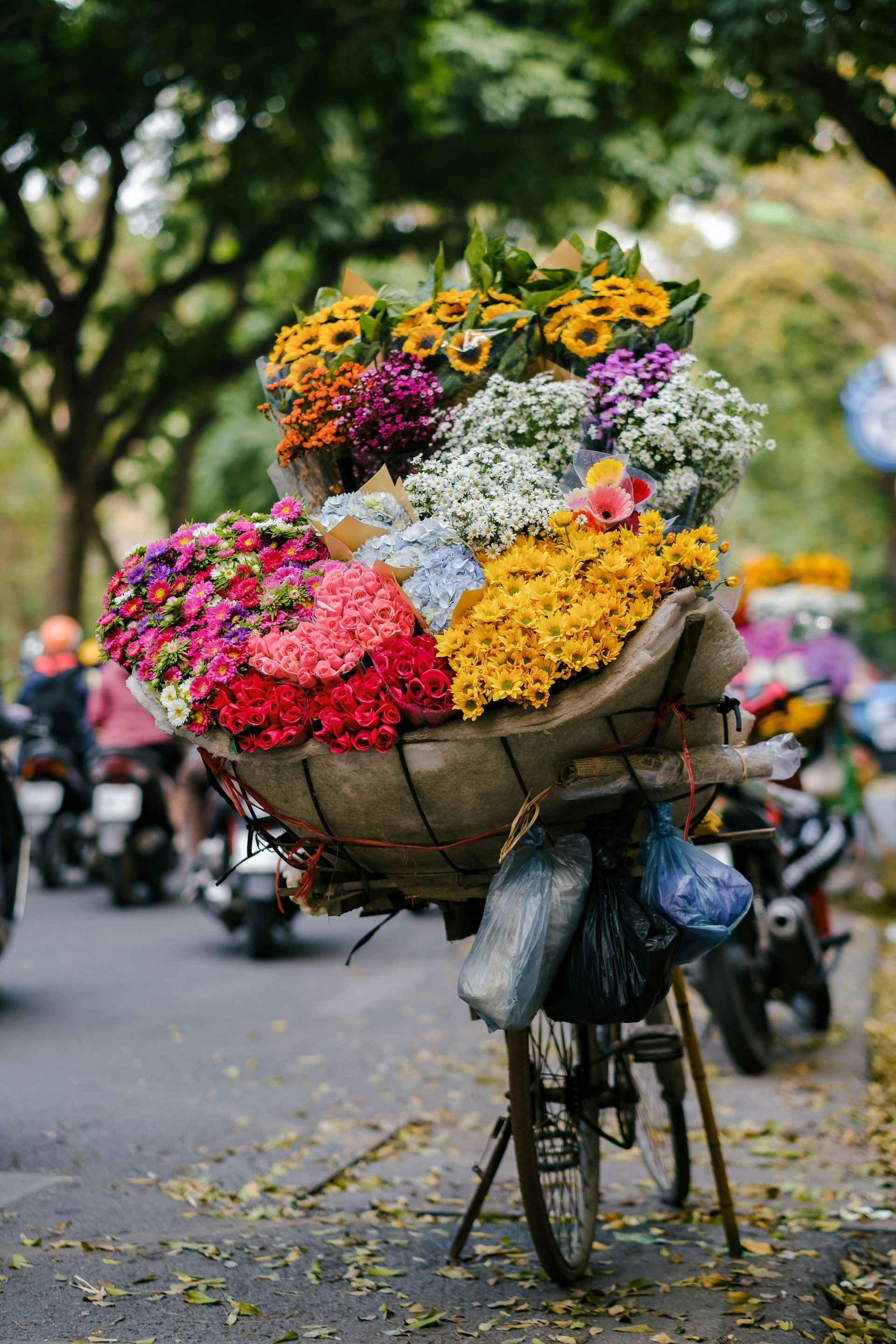 A bicycle with a large basket filled with colorful flowers, including pink, yellow, and purple blossoms, on a busy street in Vietnam.
