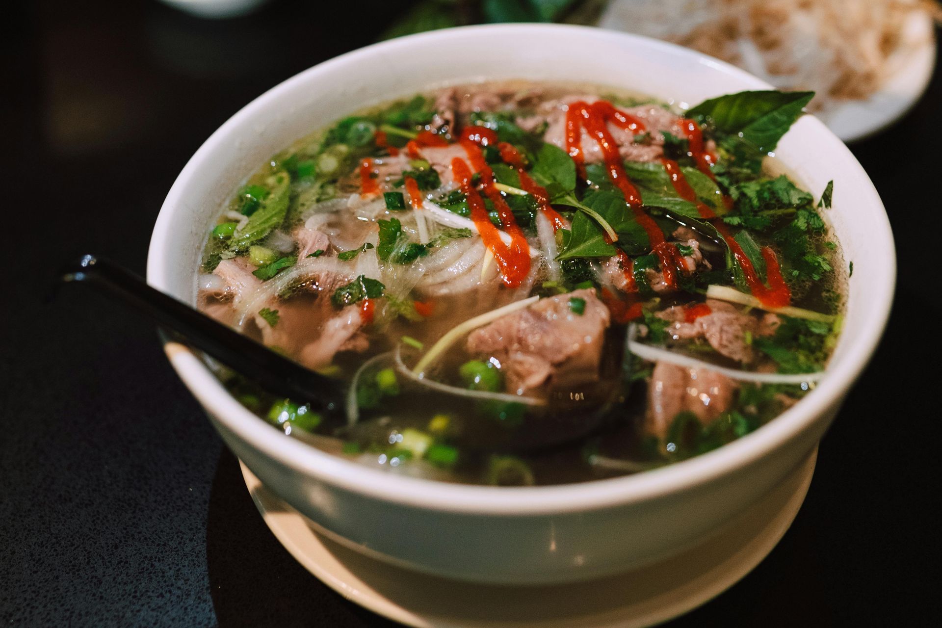 A bowl of Vietnamese pho with tender beef, fresh herbs, rice noodles, and chili slices in a steaming broth.