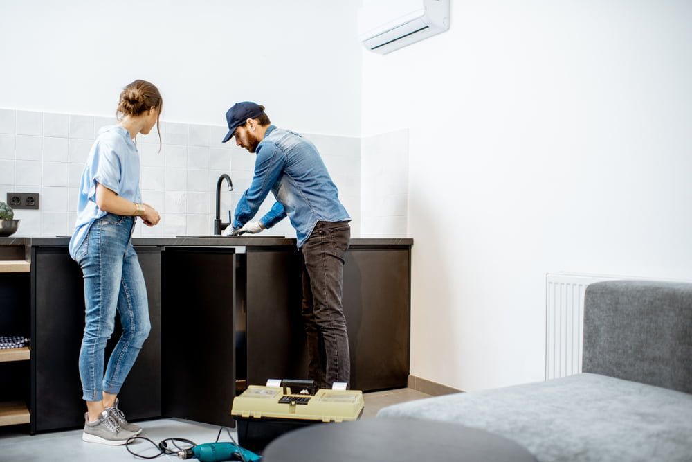 A Man and A Woman Are Fixing a Sink in A Kitchen — Custys Plumbing Services in Trinity Park, QLD