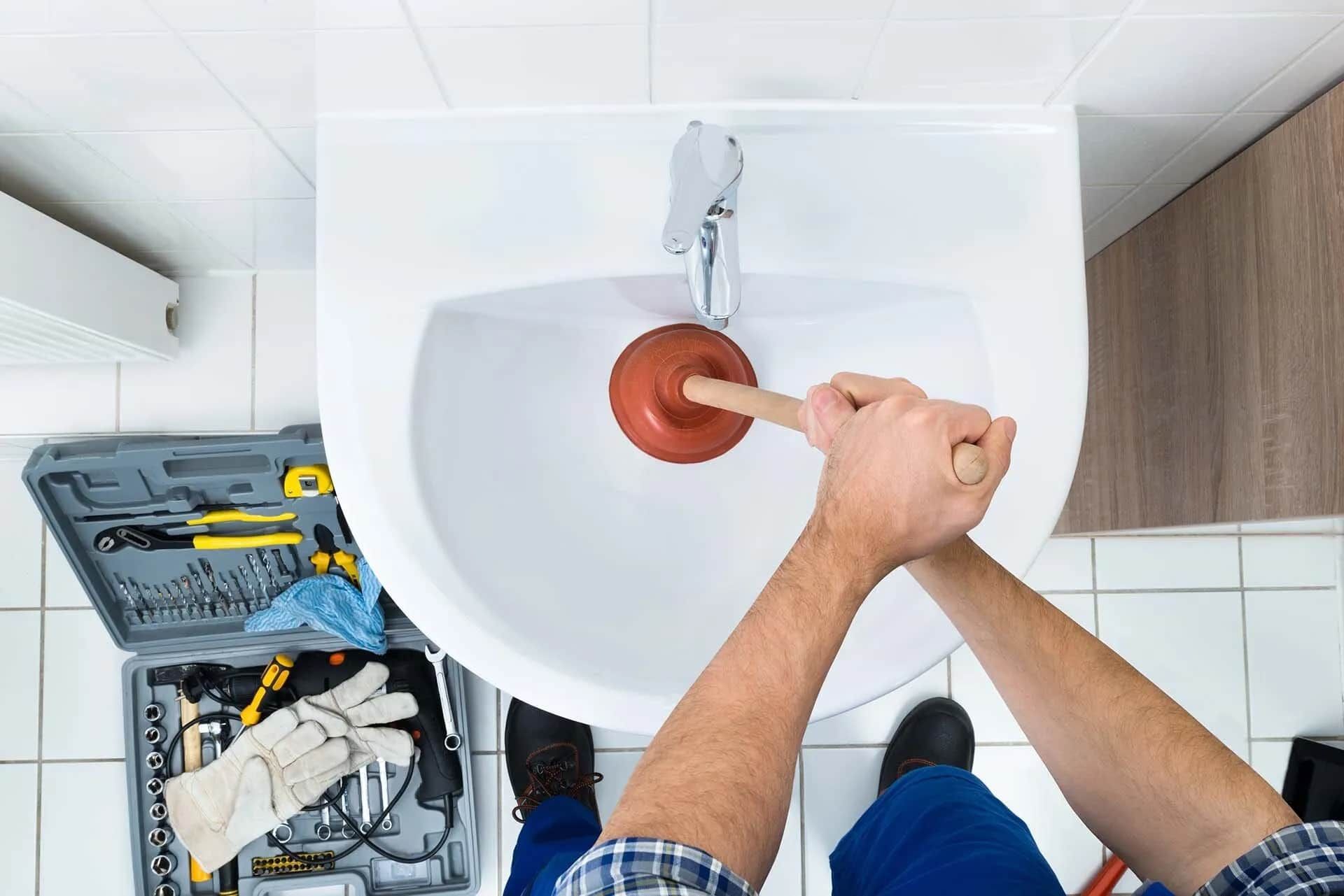 A Man Is Using a Plunger to Unblock a Bathroom Sink — Custys Plumbing Services in Trinity Park, QLD
