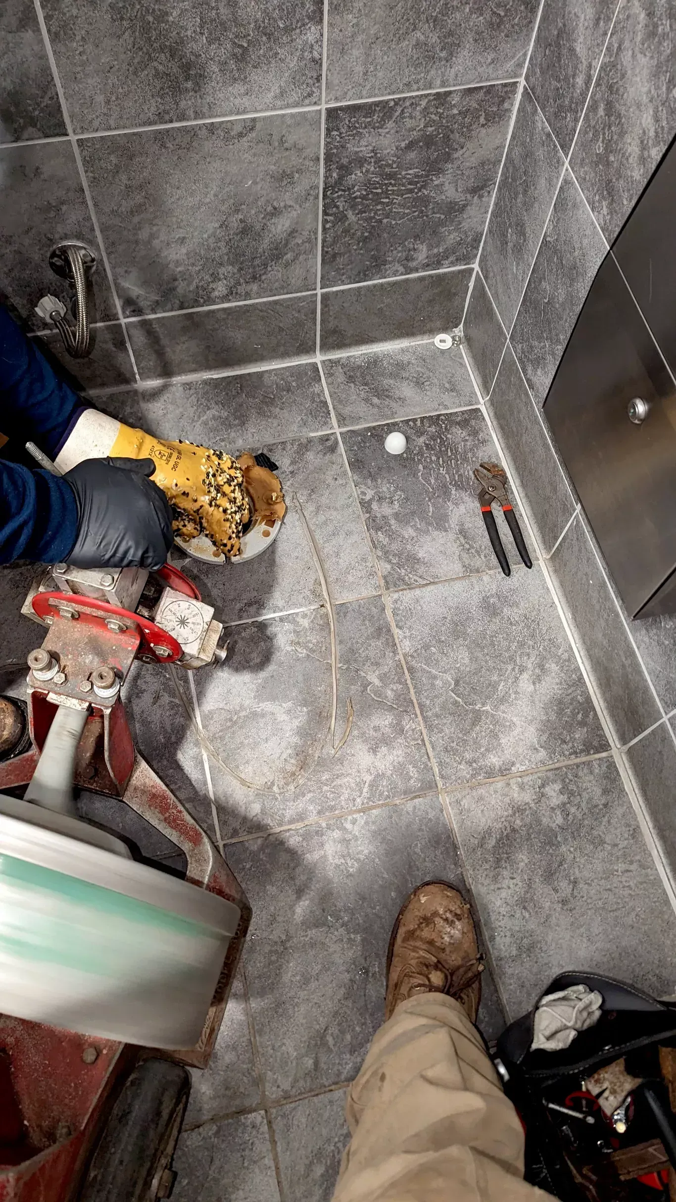 Plumber working on a pipe in a tiled bathroom. Tools and equipment visible.