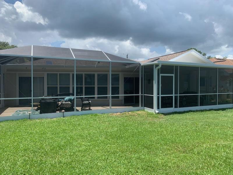 Single-story house with screened patio and large grassy yard under cloudy sky