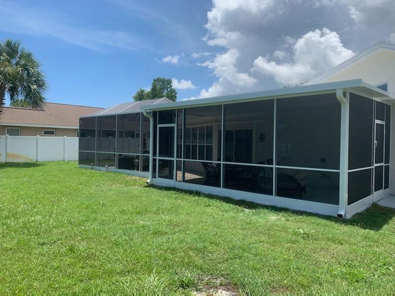 Screened patio enclosure beside a grassy backyard under a partly cloudy sky