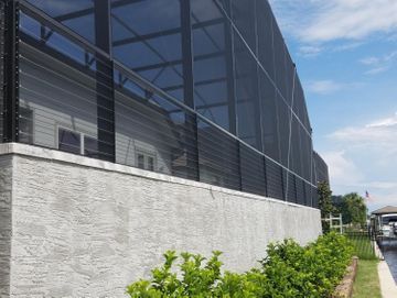 Modern building with dark glass facade, white stone wall, and green shrubs along a sidewalk