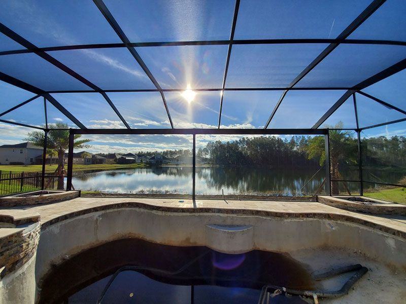Screened-in pool deck with a hot tub, overlooking a lake under a bright blue sky