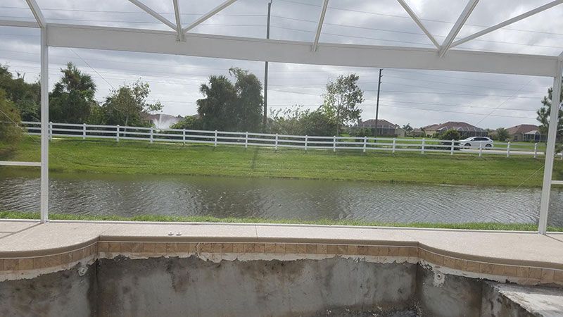Covered outdoor pool with a white fence and grassy field beyond, viewed from under a canopy