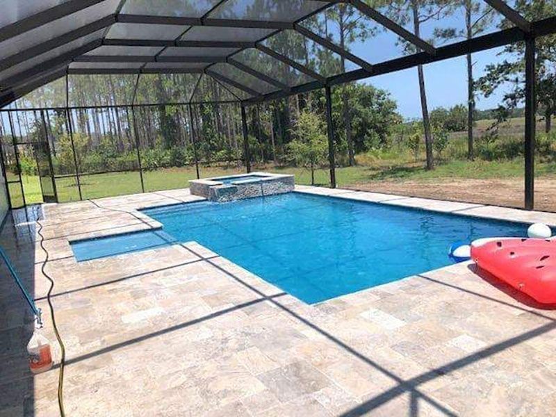 Screened backyard pool with blue water, tan deck, and red float under a metal enclosure