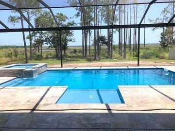 Blue swimming pool with a small spa and screened patio overlooking a grassy landscape