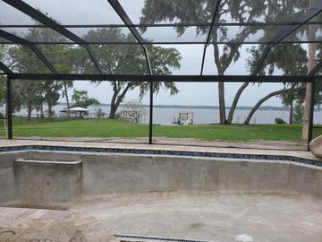 Empty concrete pool overlooking a grassy waterfront park with trees and picnic tables