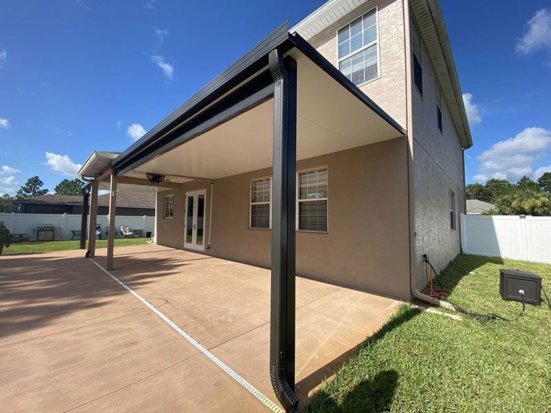 Covered patio and side view of a beige house with black support posts and a grassy yard.