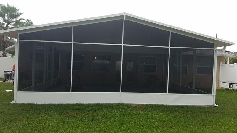 White screened porch attached to a house, with a dark roof and green lawn in front.