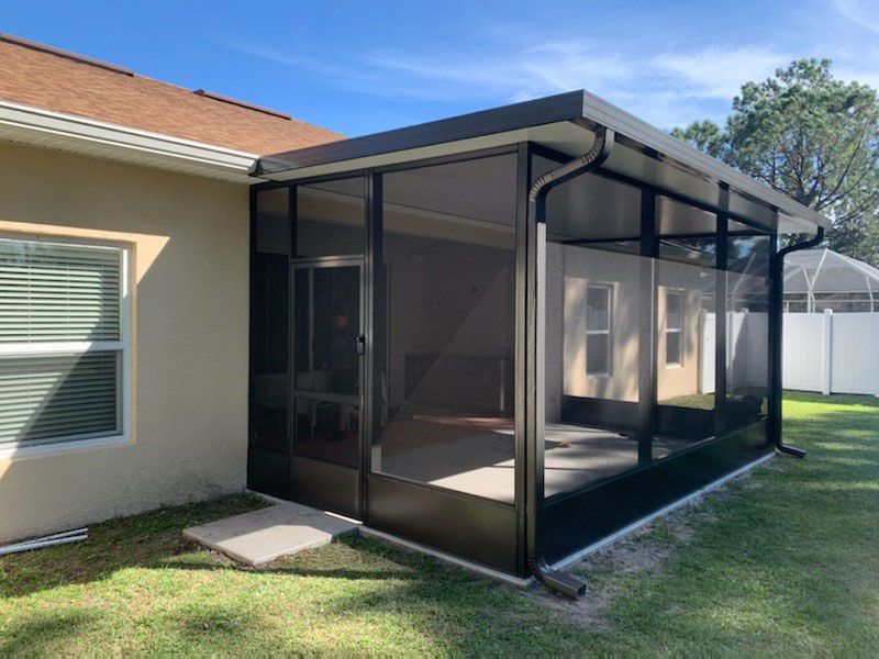 Screened patio enclosure attached to a beige house beside a grassy yard