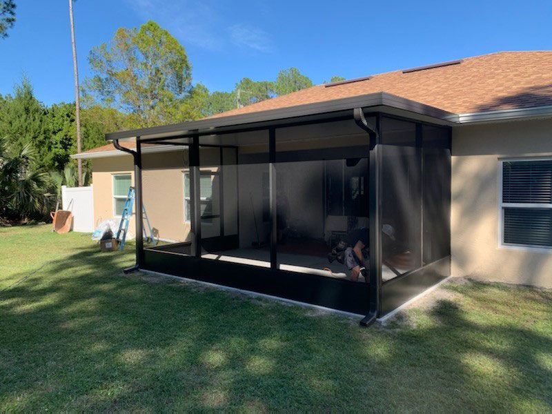 Screened patio on a suburban house with black framing and tan roof beside a grassy yard