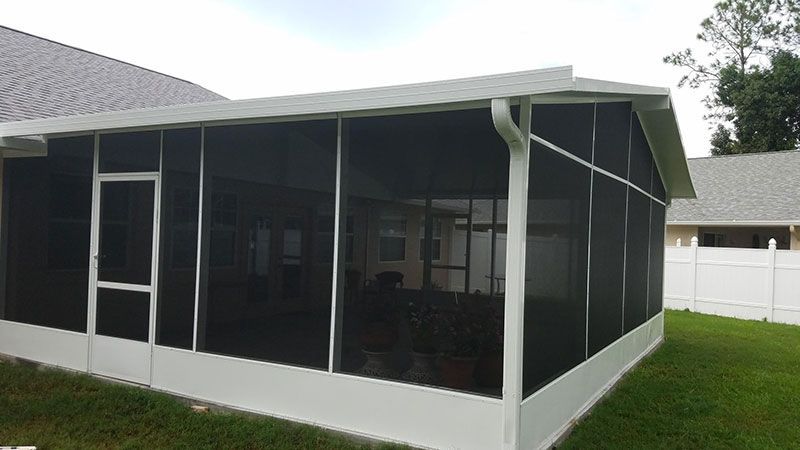 Screened porch with dark mesh panels attached to a white house on a grassy yard.