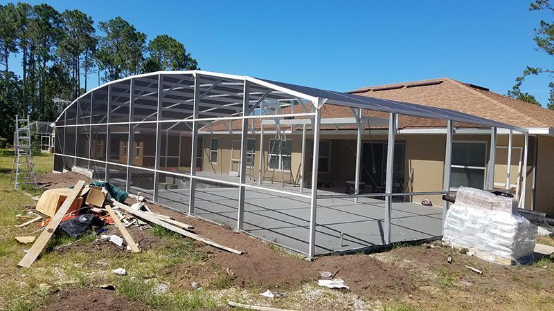 Partially framed screened porch under construction beside a house on a sunny day