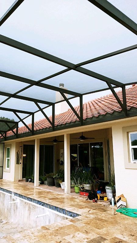 Covered patio with black metal roof frame, cream walls, red tile roof, and wet tiled floor after rain