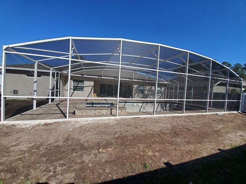 Partially built white metal frame structure on a dirt lot under a clear blue sky