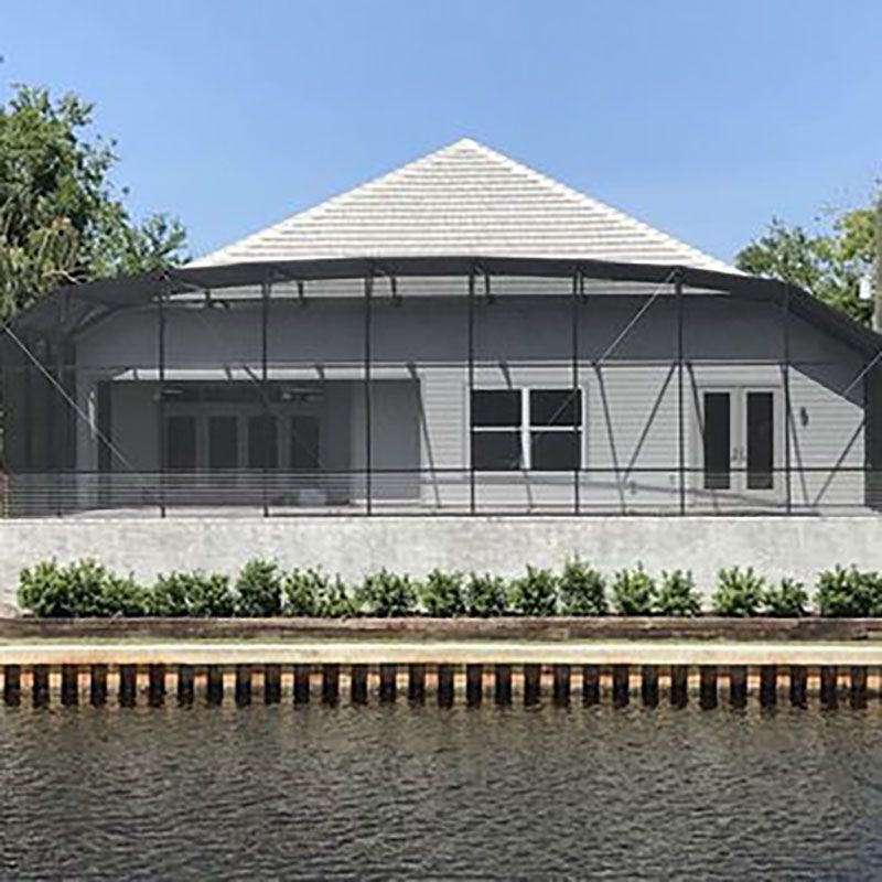 White riverside building with a tiled roof behind a low hedge and water in the foreground