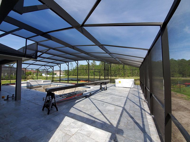 Screened patio with black metal framing, concrete floor, and a covered outdoor seating area under blue sky.