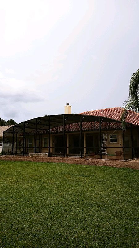 Single-story house with a red-tiled roof and screened porch beside a green lawn under a cloudy sky