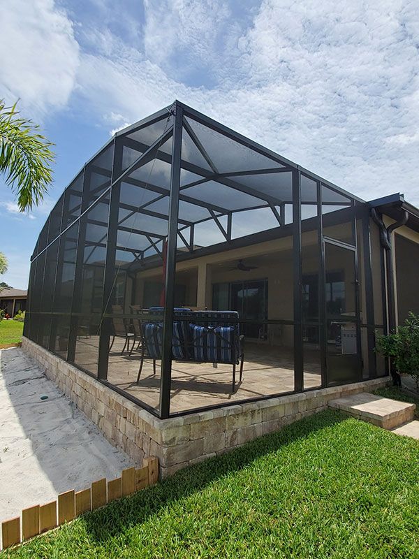 Screened patio enclosure with black metal framing on a raised brick deck beside a lawn under a blue sky