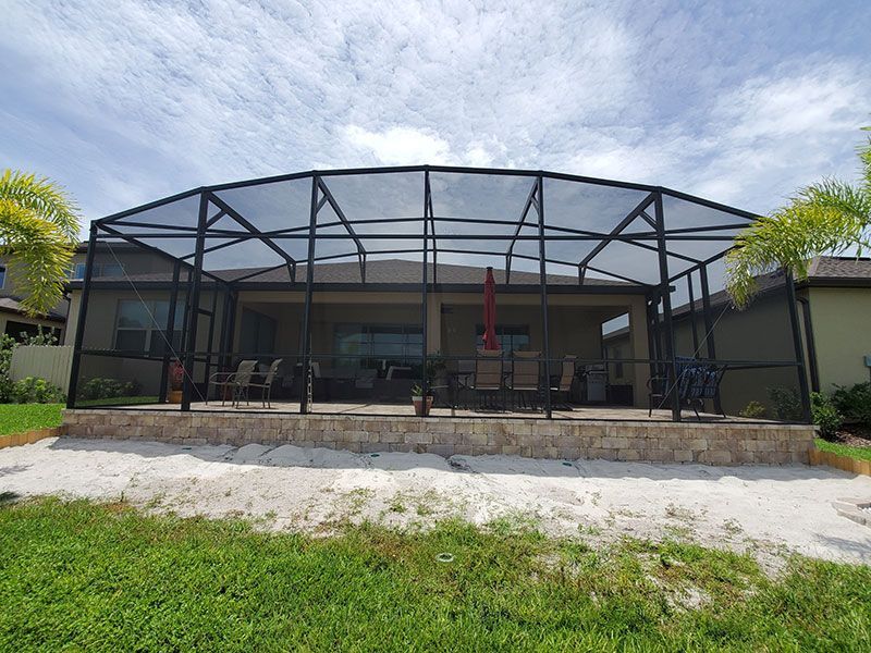 Modern screened patio with dark metal frame, chairs, and a grassy yard under a cloudy sky