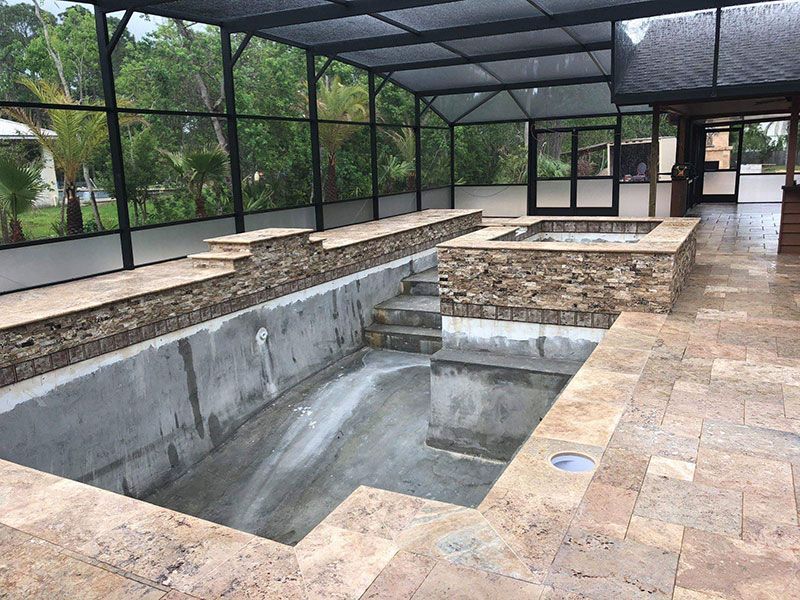 Empty covered swimming pool with tiled deck and screened enclosure, viewed from one end