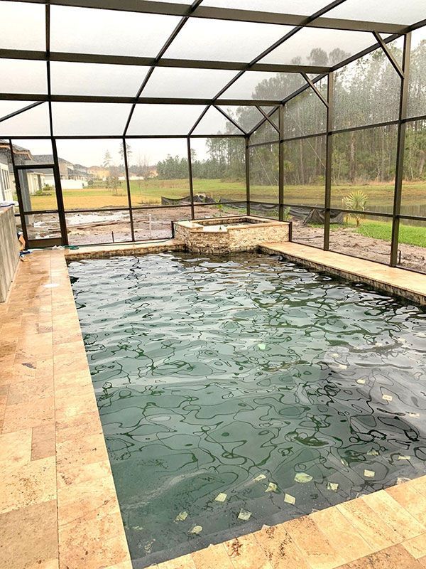 Screened-in backyard pool with murky water, stone coping, and a patio overlooking a grassy yard
