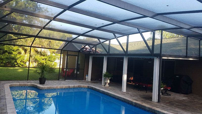 Screened pool area with blue water, brick deck, and covered patio under a metal roof
