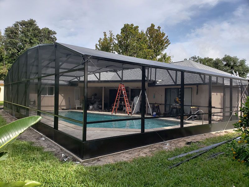 Screened-in backyard pool enclosure with a metal frame and ladder under a cloudy sky