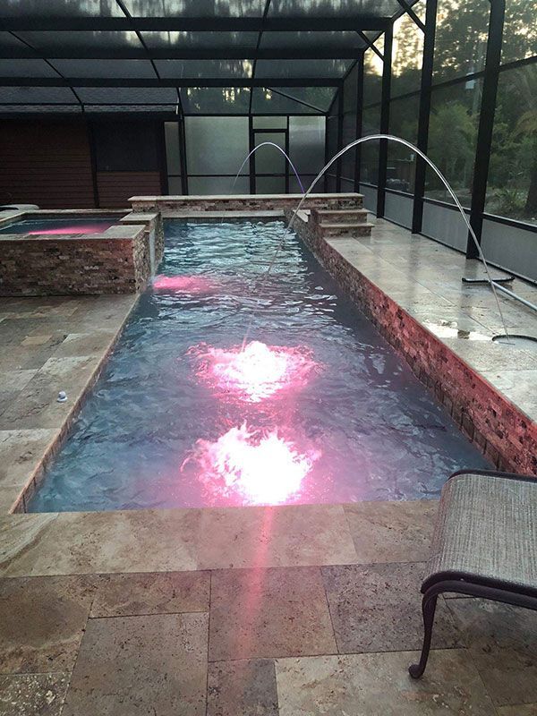 Rectangular outdoor pool under a screened enclosure, with pink light reflecting on the water.