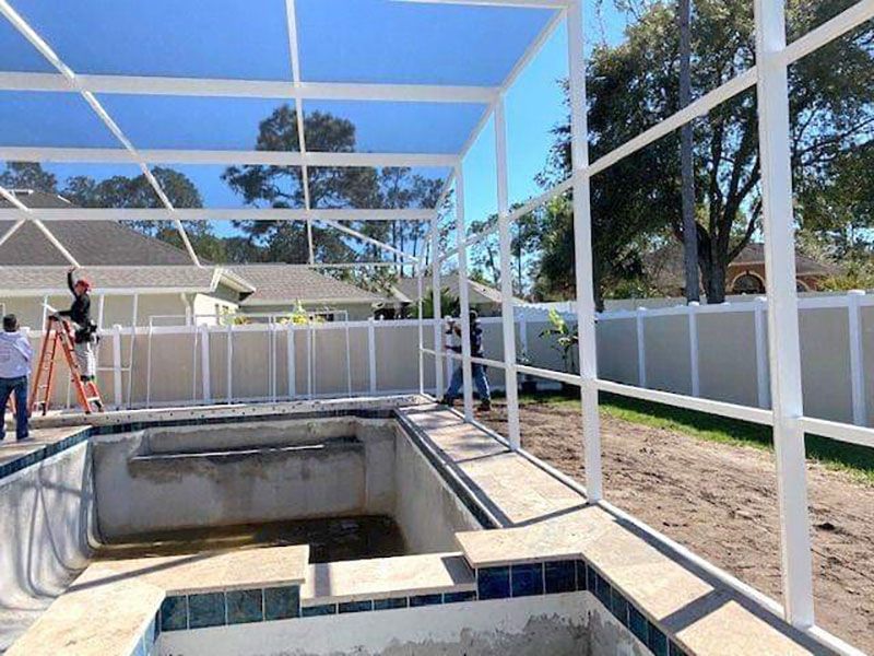 Screened backyard pool under construction with white framing and workers in the distance