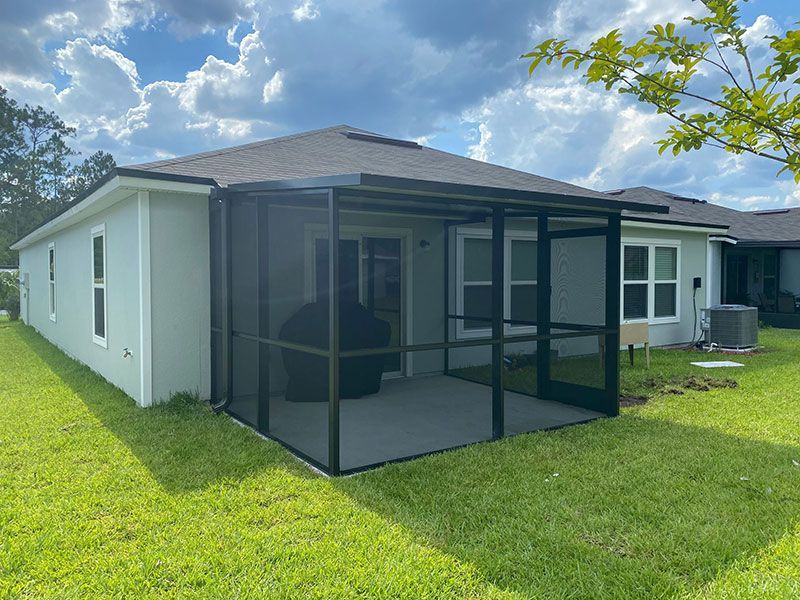 Screened porch attached to a white house with a green lawn and partly cloudy sky