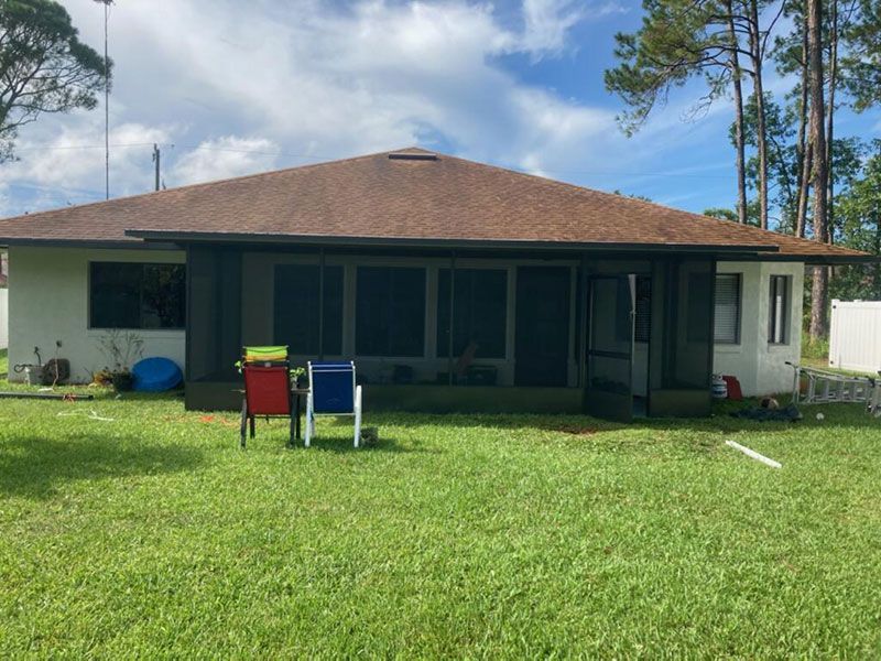 Single-story house with a large grassy yard and two lawn chairs under a covered porch.