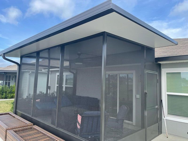 Screened patio enclosure with dark mesh panels and a sloped roof beside a house