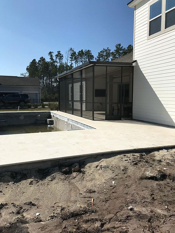 Backyard patio beside a white house with screened porch and dirt grading in front