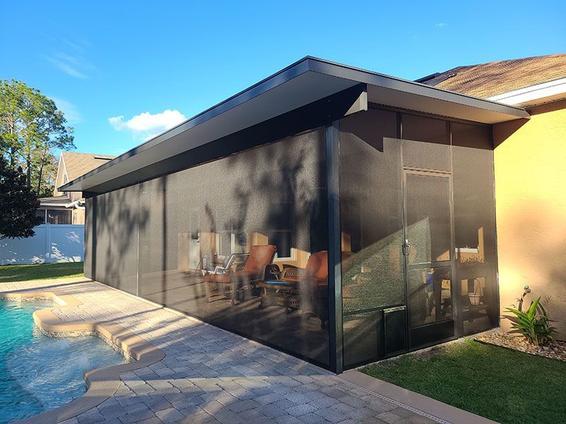 Modern screened patio beside a backyard pool with lounge chairs and glass walls