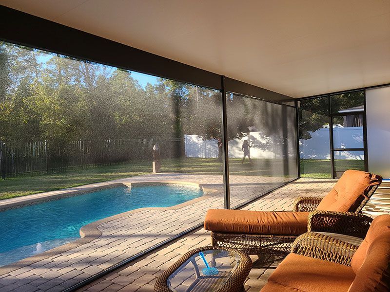 Screened patio with wicker lounge chairs overlooking a backyard pool and trees