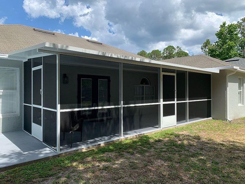 Screened patio attached to a house with dark mesh panels and a white roof in a grassy backyard
