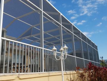 Modern glass building with a white fence, decorative lamp post, and red shrubs under a blue sky