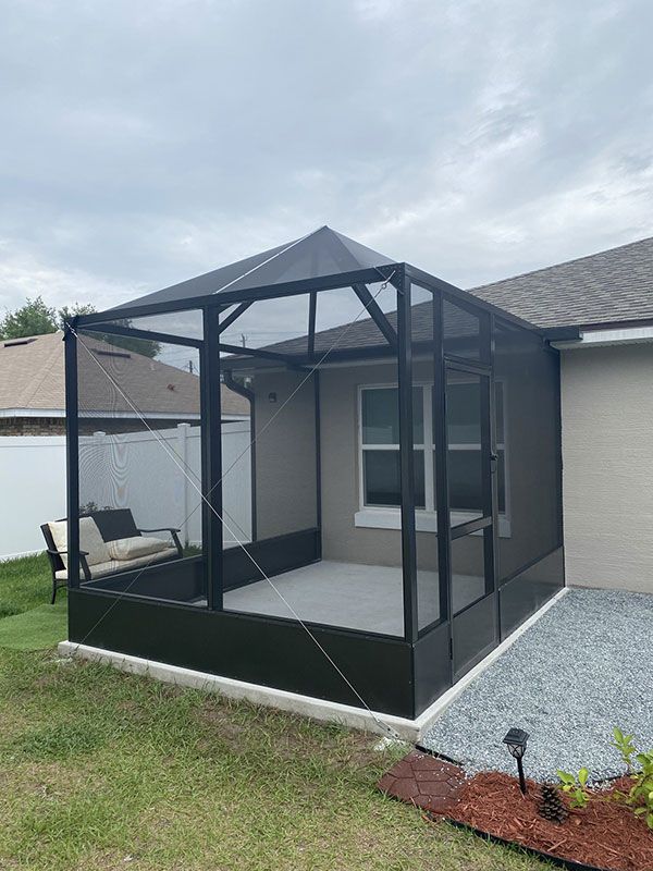 Black screened patio gazebo with peaked roof beside a house and gravel yard